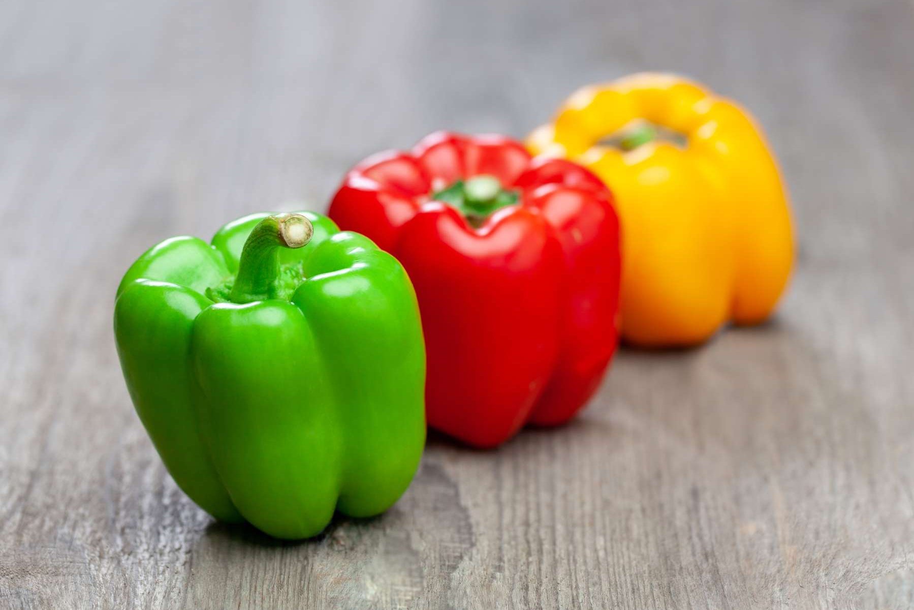 Rote, grüne und gelbe Paprika liegen auf einem Holztisch