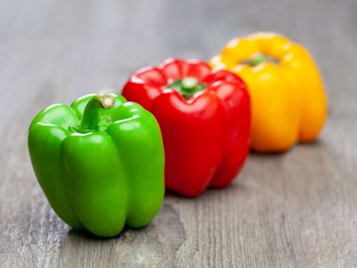 Rote, grüne und gelbe Paprika liegen auf einem Holztisch