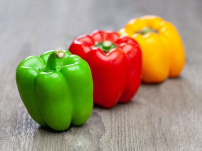 Rote, grüne und gelbe Paprika liegen auf einem Holztisch