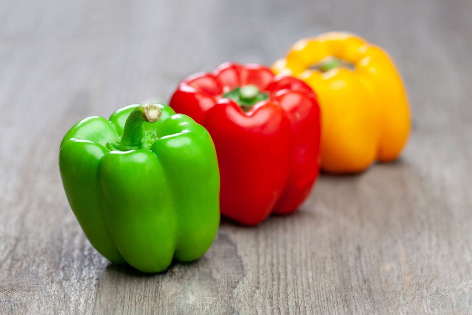 Rote, grüne und gelbe Paprika liegen auf einem Holztisch