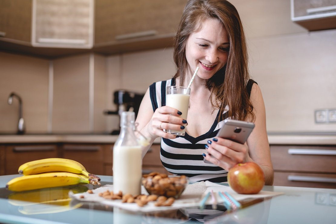 Woman drinking organic almond milk holding a phone in her hand i