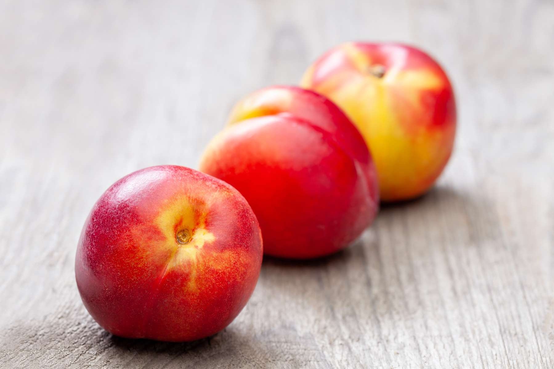 Drei Nektarinen liegen auf einem Holztisch