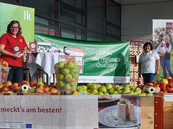 Seminarbäuerinnen und Radiomoderator vor dem Supermarkt mit Plakat und Tischen voll mit regionalen Äpfeln