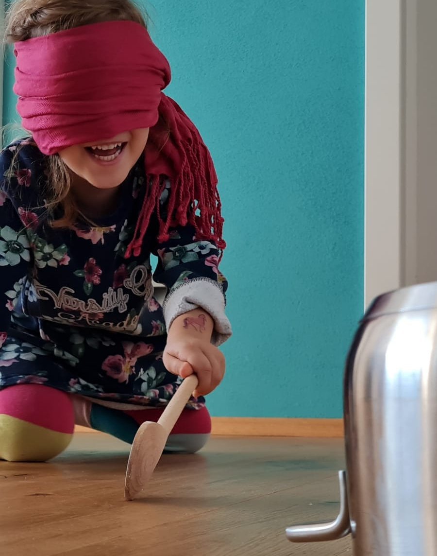 Mädchen hat Augen verbunden und Holzkochlöffel in der Hand und sucht auf Knien den Kochtopf zum Schlagen