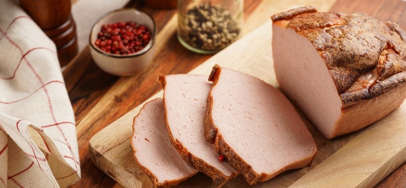 Traditional oven baked bavarian meal leberkäse sliced - meat dish made of corned beef, pork and bacon, finely ground and bakes as a bread loaf, on wooden board on dark wooden table with spices