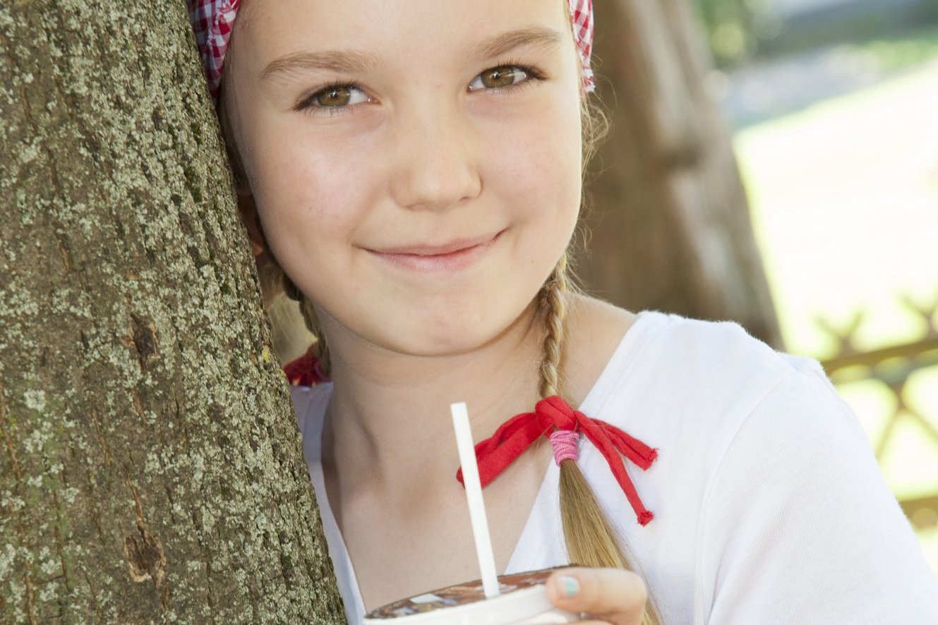 Ein Mädchen lehnt an einem Baum und hält eine Schulmilch in der Hand.