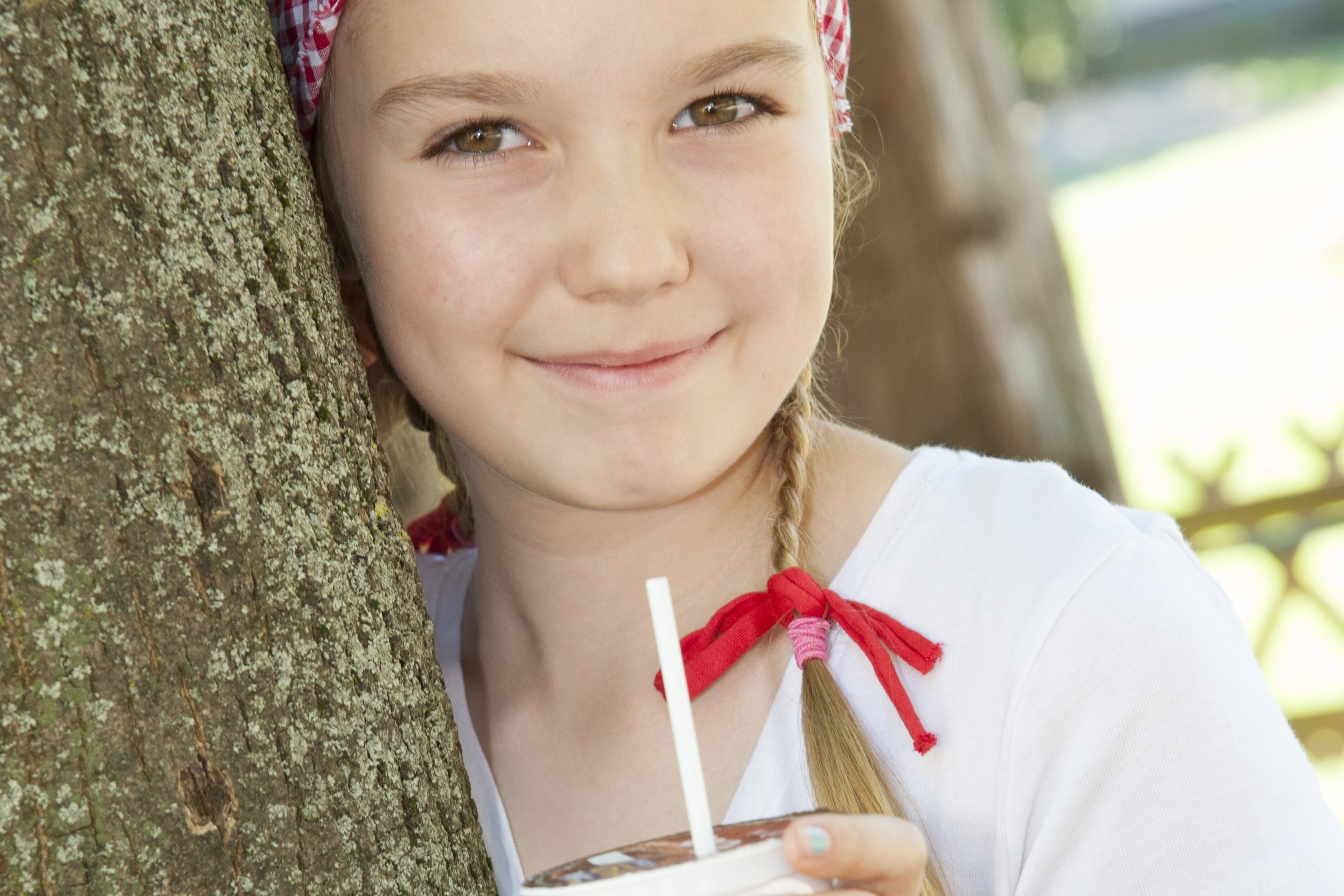 Ein Mädchen lehnt an einem Baum und hält eine Schulmilch in der Hand.