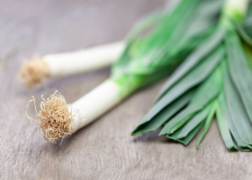 Ein paar Stangen Porree liegen auf einem Holztisch