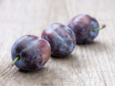 Drei Zwetschken liegen auf einem Holztisch