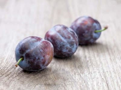 Drei Zwetschken liegen auf einem Holztisch