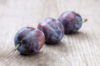 Drei Zwetschken liegen auf einem Holztisch