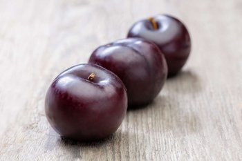 Drei Pflaumen liegen auf einem Holztisch