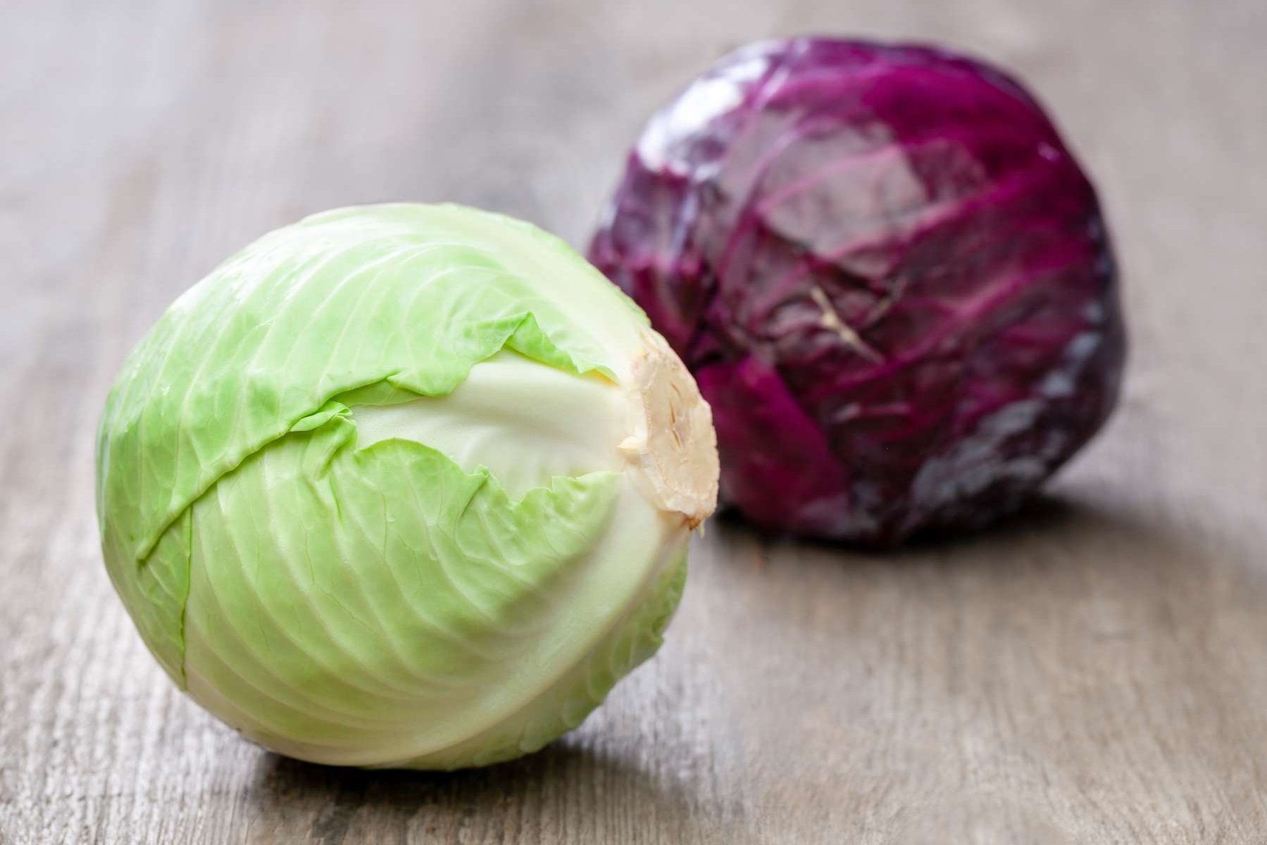 Ein Blaukraut- und ein Weißkrautkopf liegen auf einem Holztisch