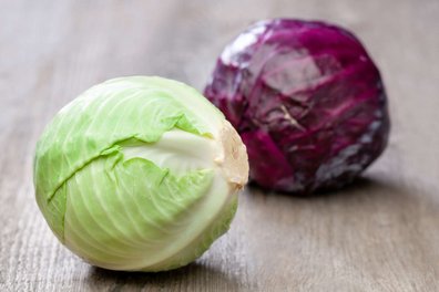 Ein Blaukraut- und ein Weißkrautkopf liegen auf einem Holztisch