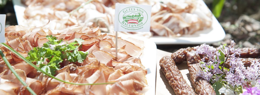 Cabanossi und Rohschinken angerichtet auf Holzbrett mit Gutes vom Bauernhof-Logo