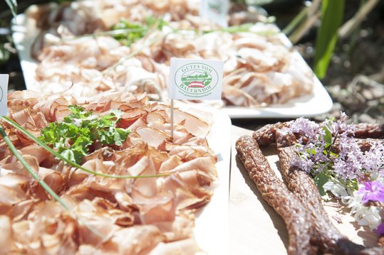 Cabanossi und Rohschinken angerichtet auf Holzbrett mit Gutes vom Bauernhof-Logo