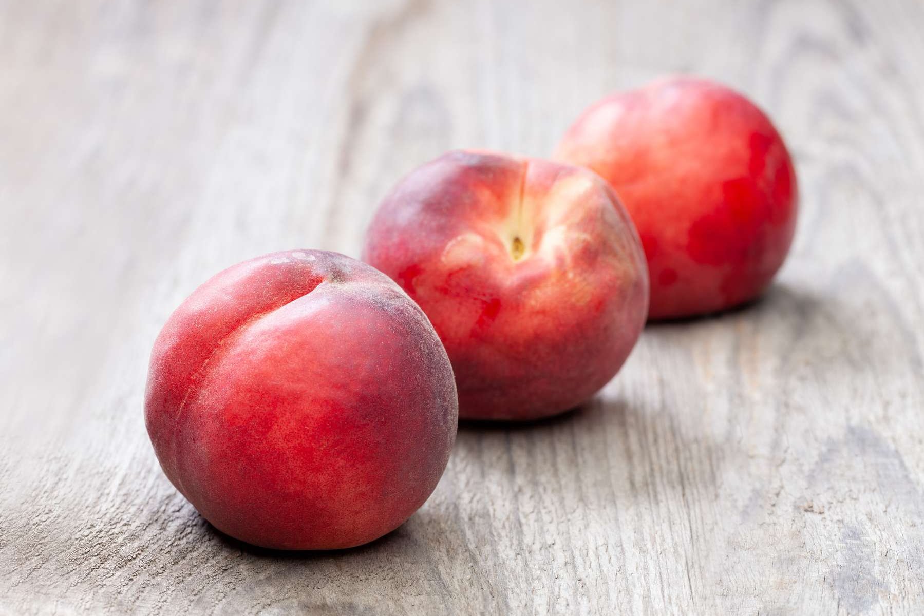 Drei Pfirsiche liegen auf einem Holztisch