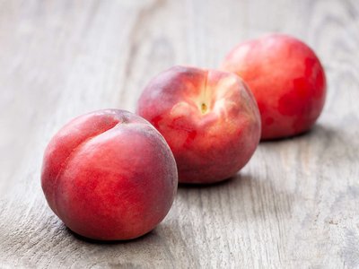 Drei Pfirsiche liegen auf einem Holztisch