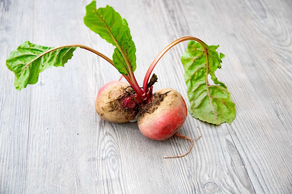 Zwei Rote Rüben mit Blättern auf Holztisch