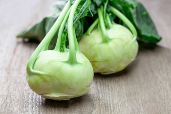 Zwei Kohlrabiköpfe liegen auf einem Holztisch