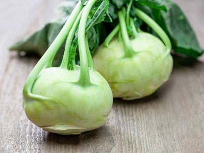 Zwei Kohlrabiköpfe liegen auf einem Holztisch