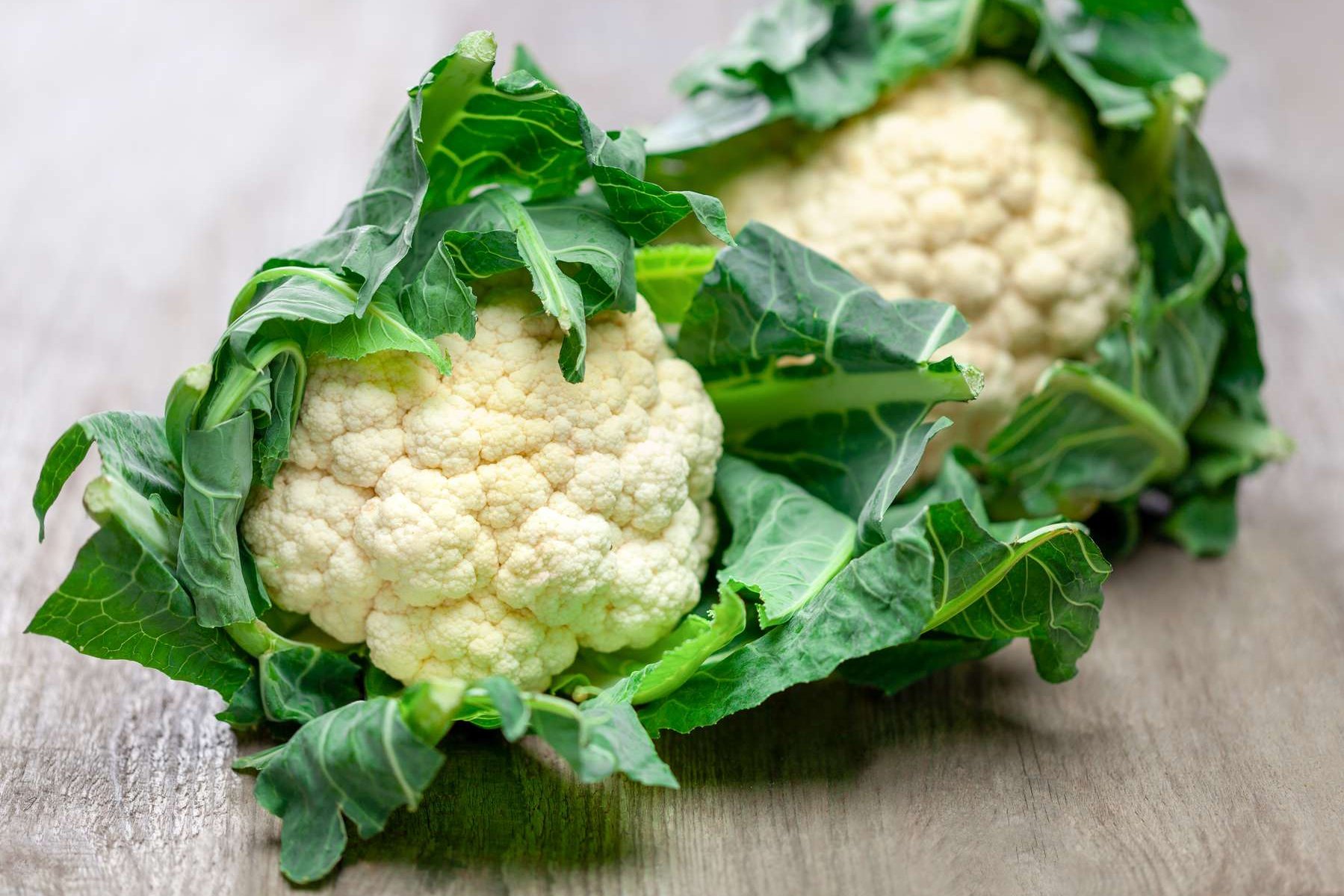 Zwei Karfiolköpfe liegen auf einem Holztisch