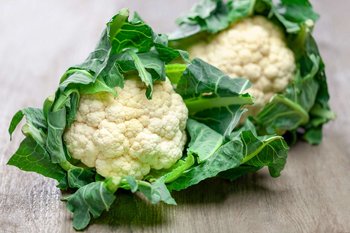 Zwei Karfiolköpfe liegen auf einem Holztisch