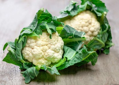 Zwei Karfiolköpfe liegen auf einem Holztisch