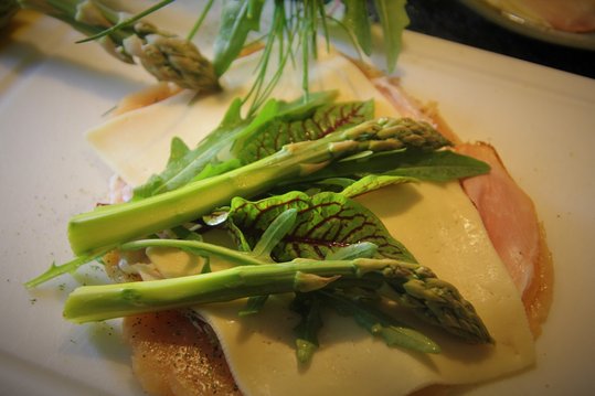 Die Schnitzerl gut würzen und mit 2 Stück Schinkenscheiben, 2 Stück Käsescheiben, 2 Stangen grünem Spargel und frischen Kräutern belegen.