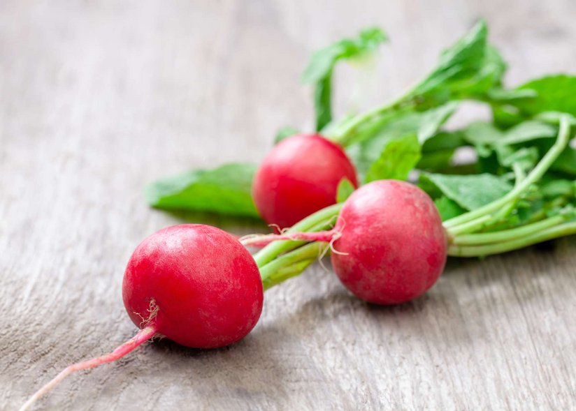 Ein paar Radieschen liegen auf einem Holztisch