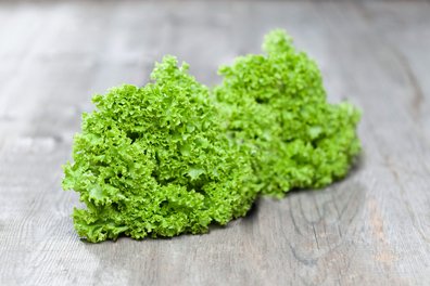 Zwei Salatköpfe liegen auf einem Holztisch