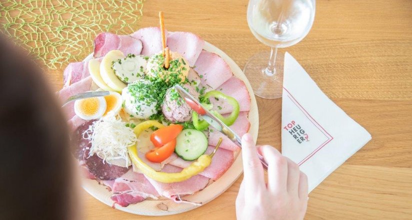 Heurigen-Jausenplatte und Weinglas - Gast wartet mit erhobener Gabel, um es genießen zu können