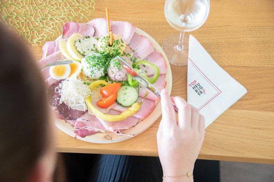 Heurigen-Jausenplatte und Weinglas - Gast wartet mit erhobener Gabel, um es genießen zu können