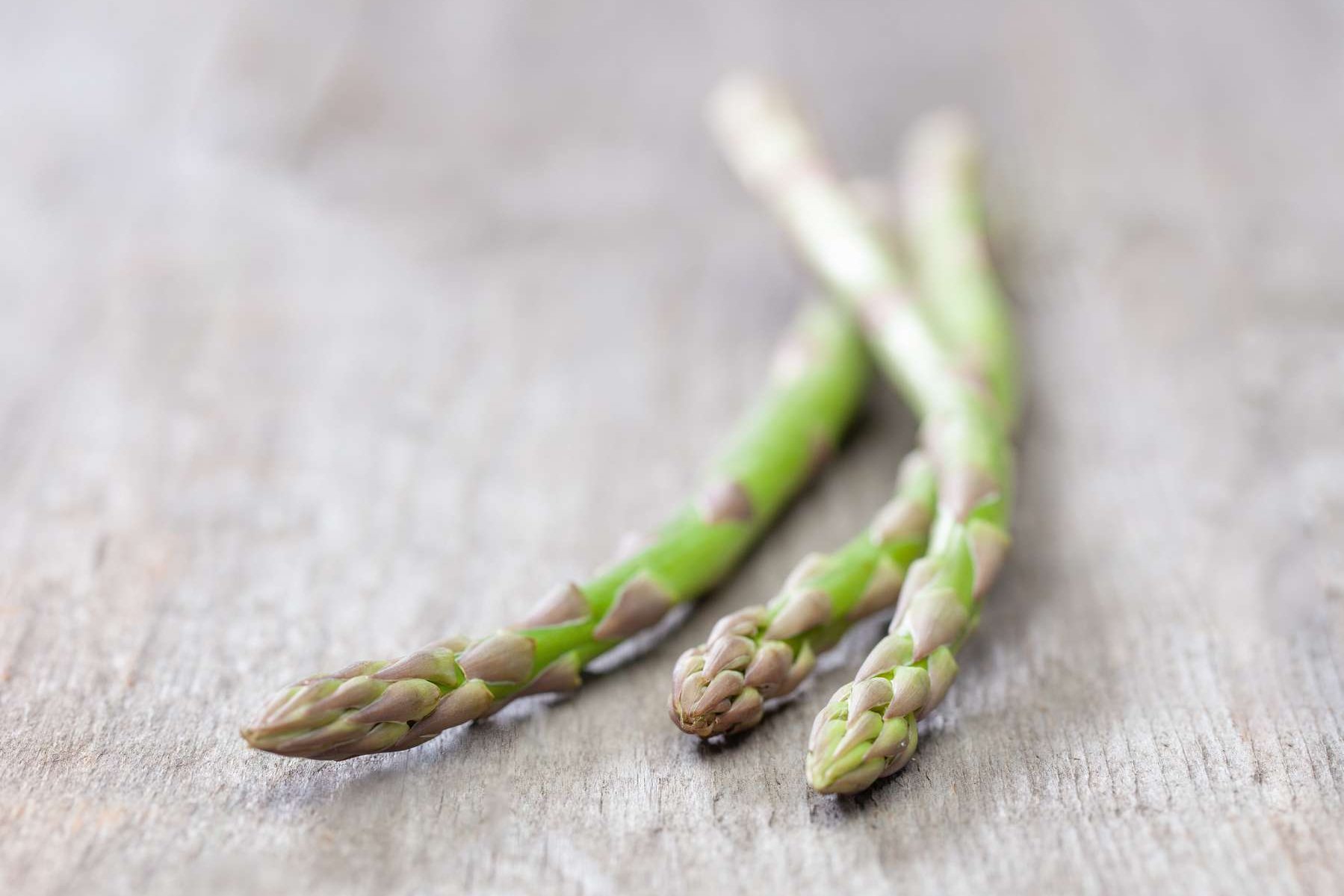Drei Stangen grüner Spargel liegen auf einem Holztisch