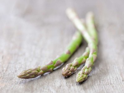 Drei Stangen grüner Spargel liegen auf einem Holztisch