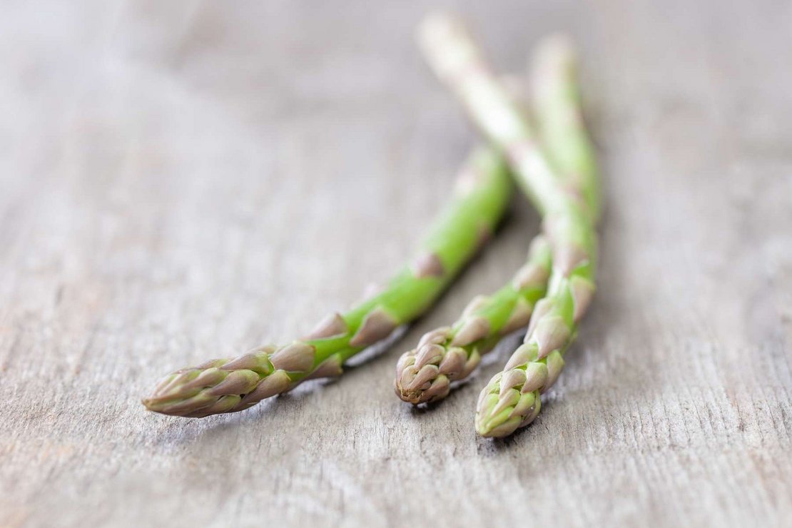 Drei Stangen grüner Spargel liegen auf einem Holztisch