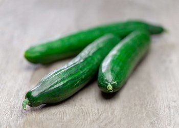 Drei Gurken liegen auf einem Holztisch