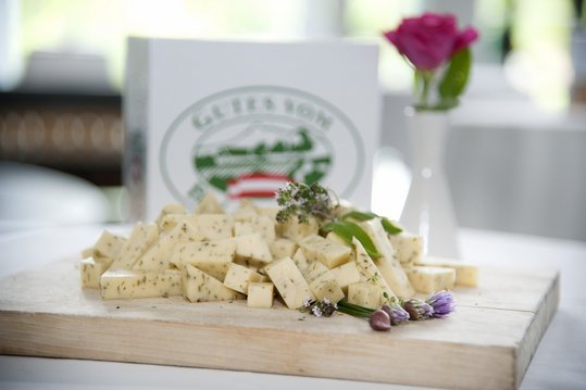 Käse angerichtet auf Holzbrett vor Gutes vom Bauernhof-Logo