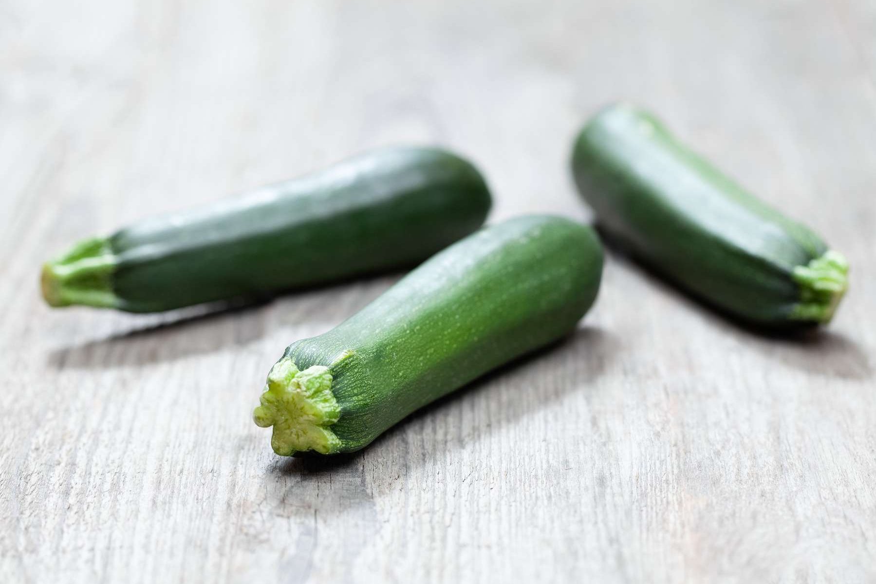 Drei Zucchini liegen auf einem Holztisch