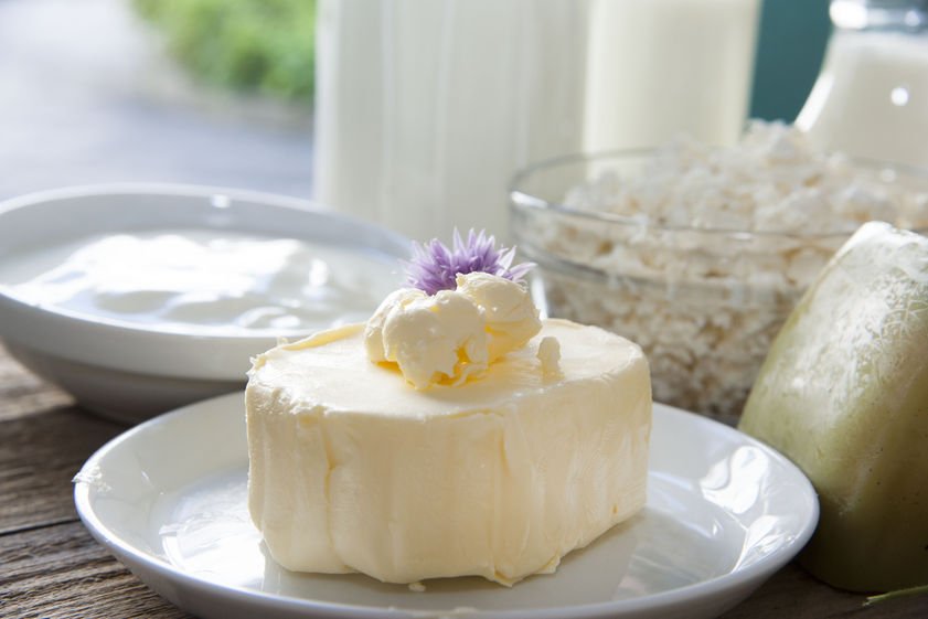 Butter liegt dekoriert auf Teller neben Käse, Topfen, Milch und anderen Milchprodukten