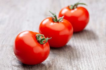 Drei Paradeiser liegen auf einem Holztisch