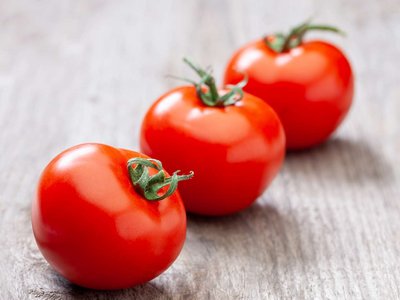 Drei Paradeiser liegen auf einem Holztisch