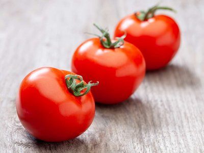 Drei Paradeiser liegen auf einem Holztisch