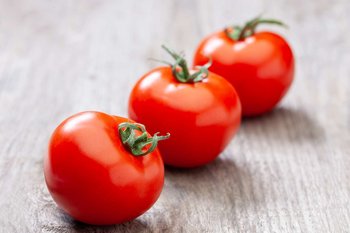 Drei Paradeiser liegen auf einem Holztisch