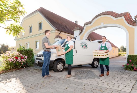 Drei Personen - ein Konsument mit Bauer und Bäuerin - vor Gutes vom Bauernhof-Betrieb. 