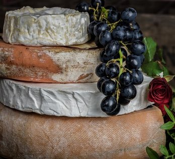 Hartkäse, Weichkäse, Schimmelkäse sind übereinander gestapelt, darauf liegt eine Weintraube und daneben ein Bund Rosen