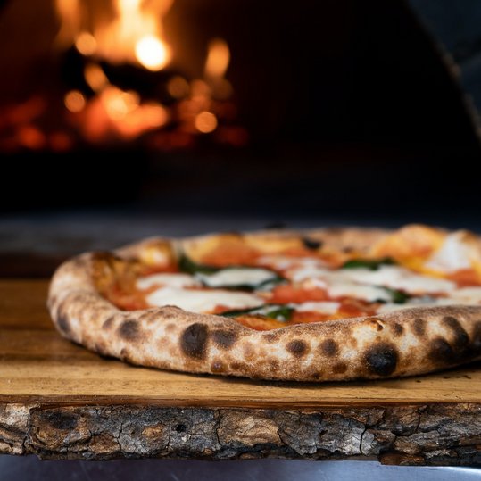 Neapoletanische Pizza auf Holzbrett vor Steinofen