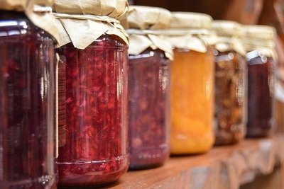 Mehrere unterschiedlich gefüllte Marmeladegläser stehen verschlossen auf einem Holzbrett