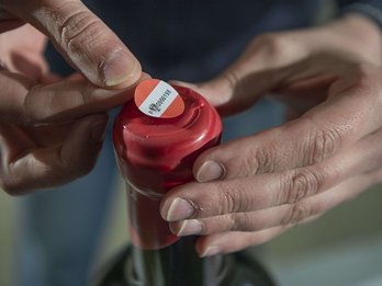 Mann bringt rot-weiß-rote Weinbanderole auf Flasche mit Wachsverschluss an.