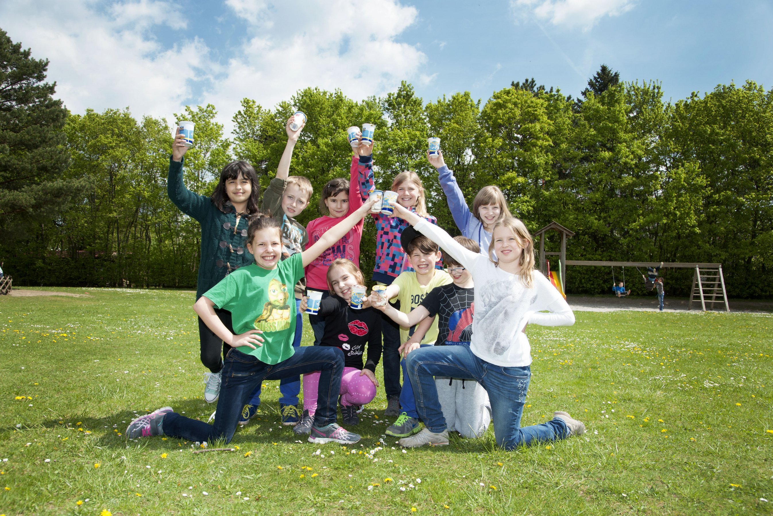 Eine paar Kinder knien in der Wiese und halten ihre Schulmilch hoch.